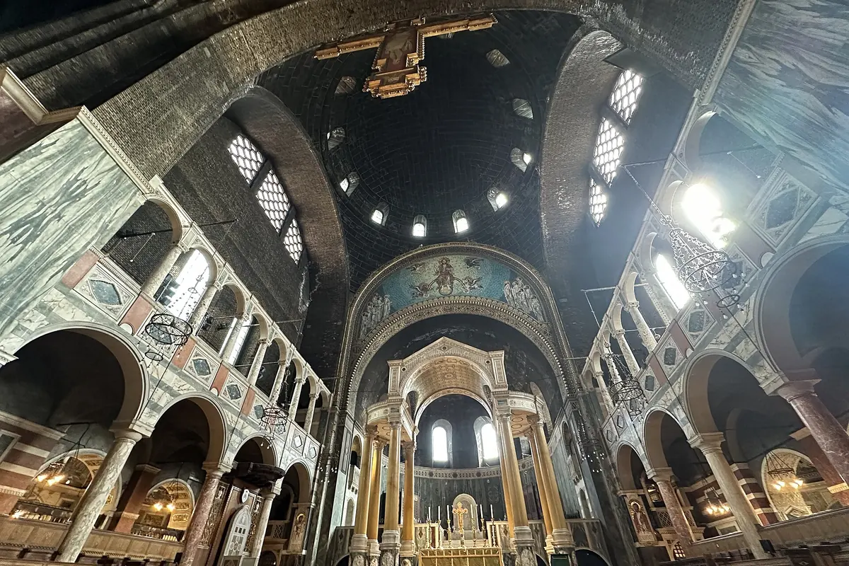 Vista ascendente del interior de la catedral hacia una cúpula oscura de ladrillo perforada por pequeñas ventanas, sobre arcadas de mármol a rayas y un arco elevado.