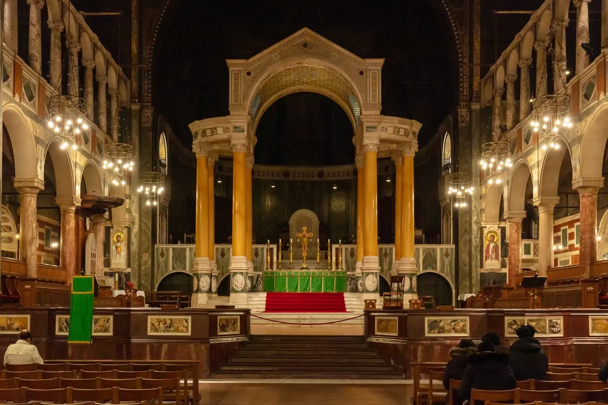 El santuario de Westminster Cathedral, con columnas de mármol amarillo que sostienen el baldaquino sobre el altar mayor, arcadas a ambos lados y un ábside oscuro al fondo.